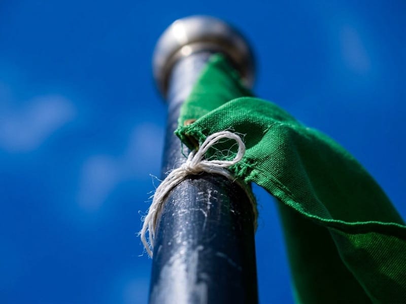 Green cloth flag tied with twine to a dark pole against a clear blue sky