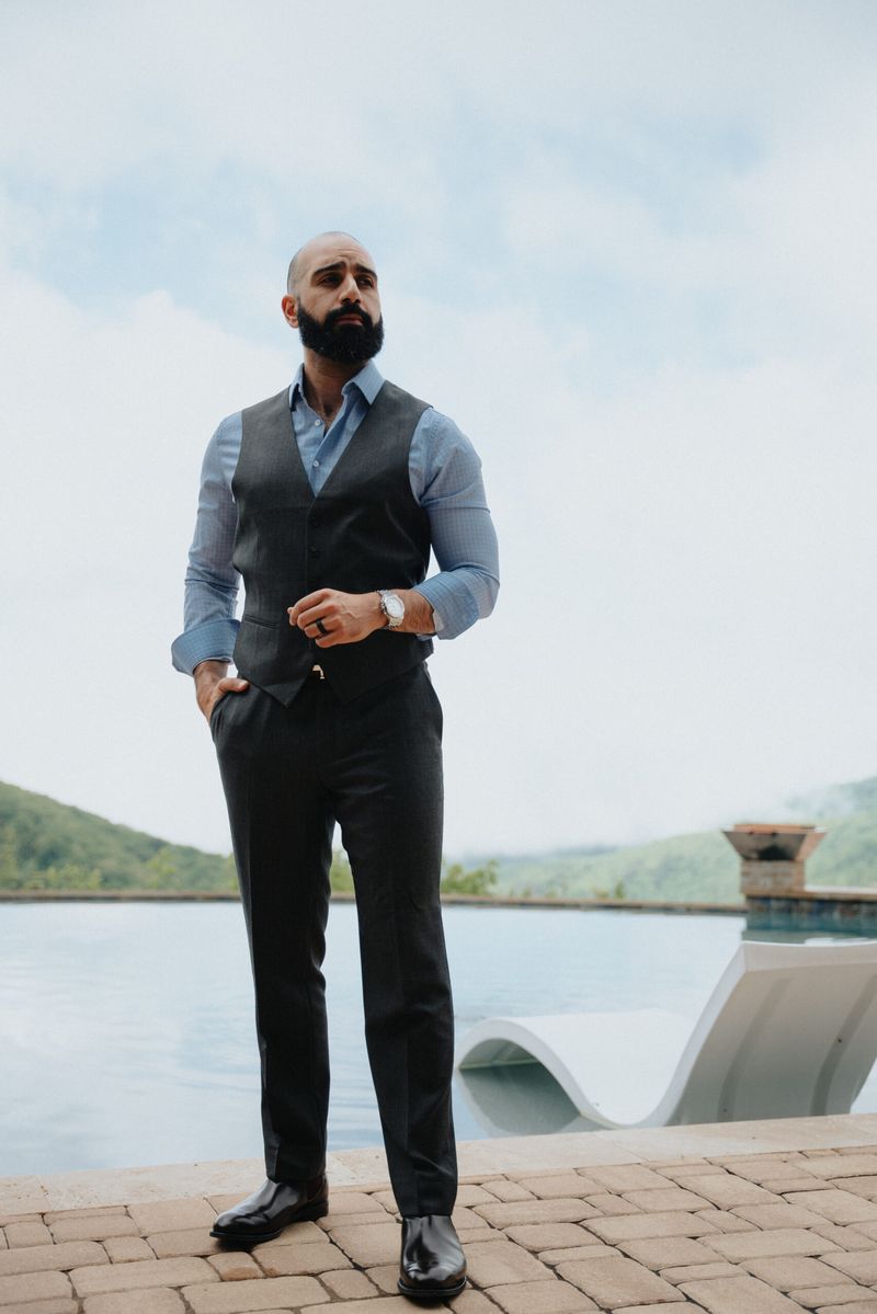 Full-length portrait of Ayman Al-Abdullah in a vest and dress shirt standing beside an infinity pool with hills behind