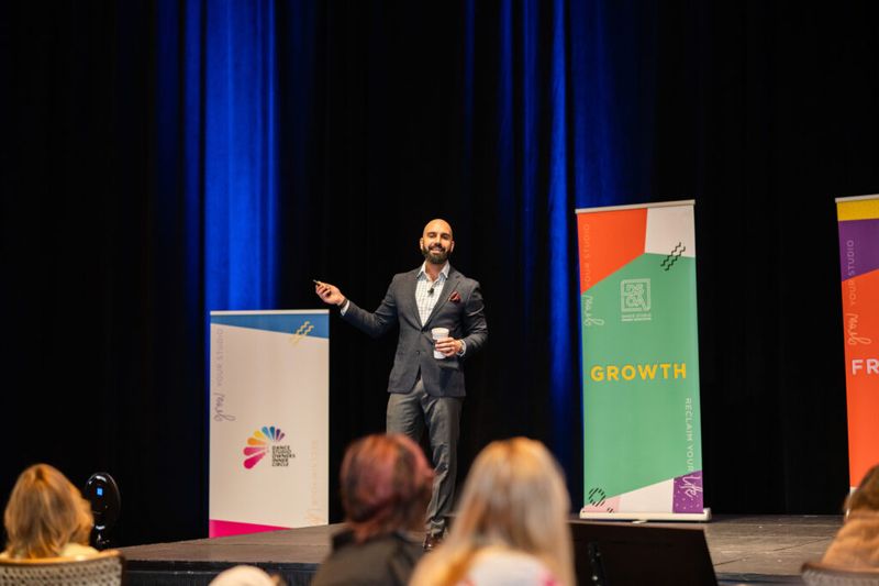 Ayman Al-Abdullah speaking on stage beside Growth and Dance Studio Owners Inner Circle banners
